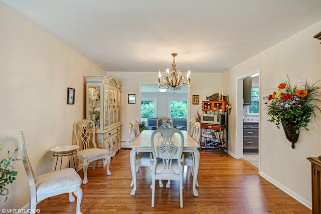 dining room featuring a chandelier, light wood finished floors, baseboard heating, and baseboards