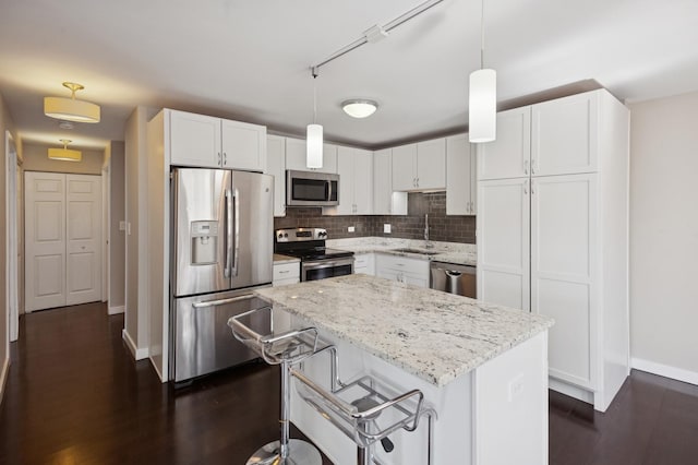 kitchen featuring stainless steel appliances, a sink, baseboards, light stone countertops, and white cabinets