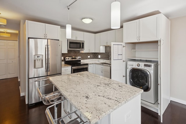 kitchen with stainless steel appliances, washer / clothes dryer, baseboards, light stone counters, and a center island