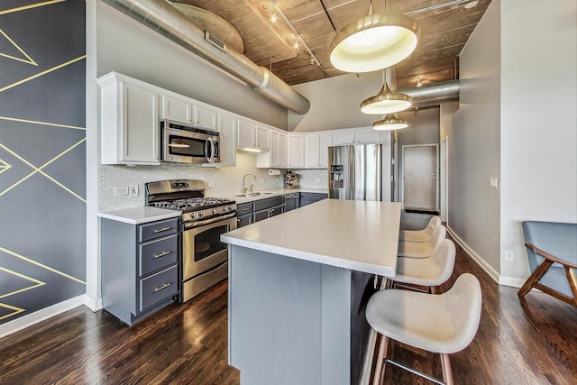 kitchen with stainless steel appliances, a sink, dark wood-style floors, a center island, and a towering ceiling