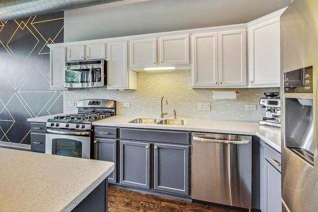 kitchen with stainless steel appliances, a sink, gray cabinets, light countertops, and tasteful backsplash