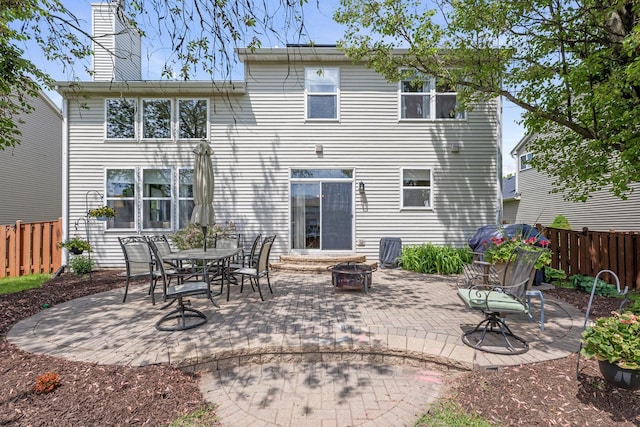 rear view of property featuring a fire pit, fence, a chimney, and a patio