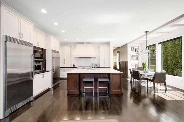 31 Concord Dr, Oak Brook, IL 60523 - kitchen featuring built in appliances, custom range hood, dark wood finished floors, white cabinets, and an island with sink