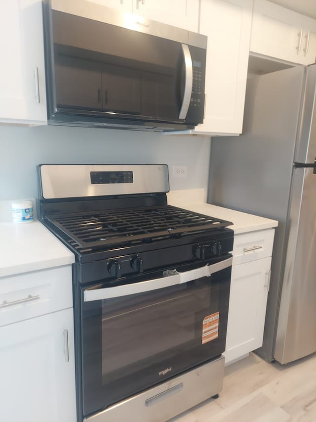 kitchen with stainless steel appliances, light countertops, white cabinets, and light wood-type flooring