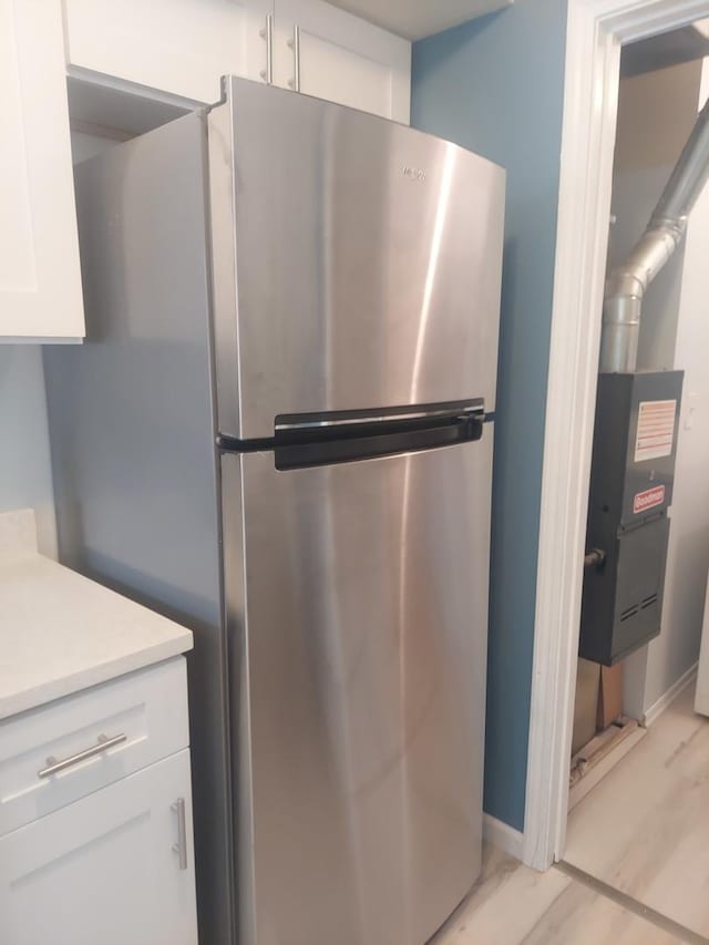 kitchen with freestanding refrigerator, white cabinets, light countertops, baseboards, and light wood-type flooring
