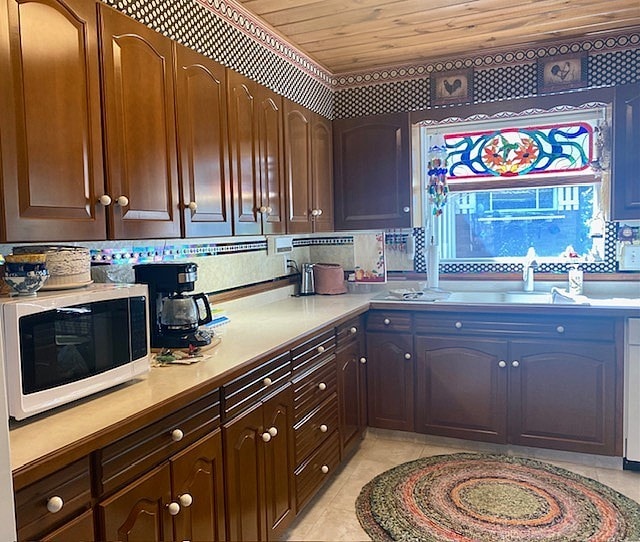 kitchen featuring white microwave, light countertops, a sink, wood ceiling, and light tile patterned floors