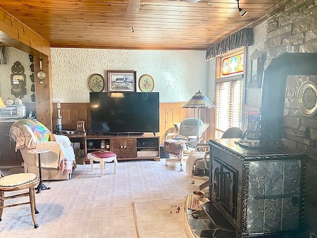 living area featuring a wood stove, wooden ceiling, wainscoting, a textured wall, and wooden walls
