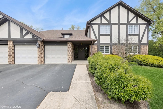 tudor home featuring brick siding, stucco siding, and driveway