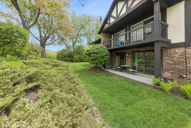 view of grassy yard featuring a balcony and a patio