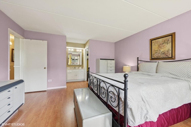 bedroom with light wood finished floors, ensuite bath, and baseboards