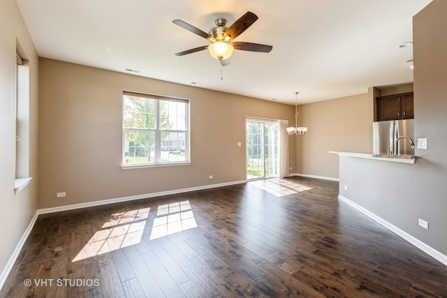unfurnished living room featuring a chandelier, a ceiling fan, dark wood-type flooring, and baseboards