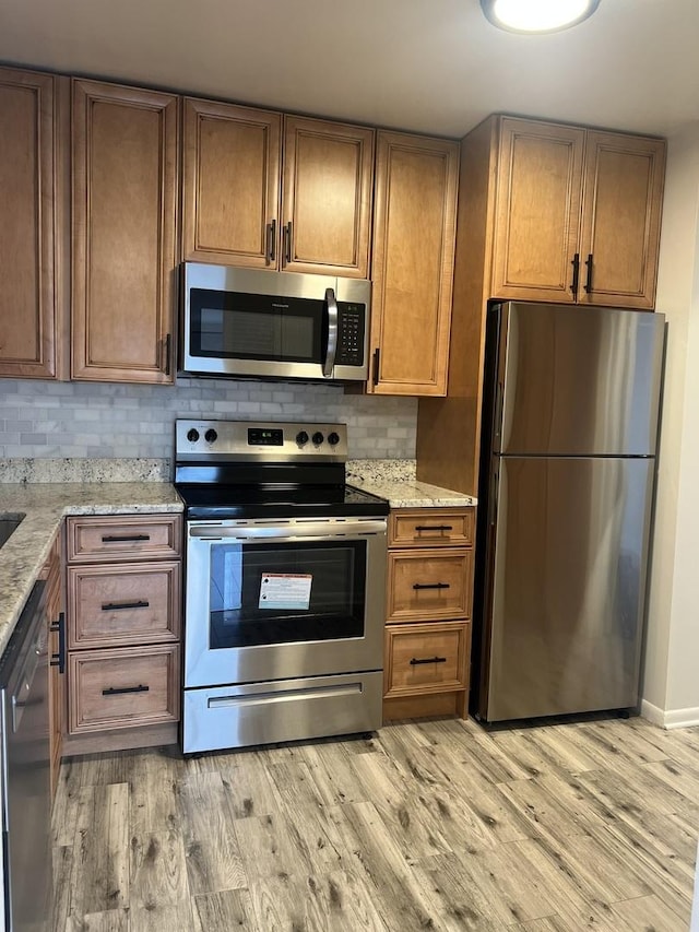 kitchen with appliances with stainless steel finishes, light wood-style floors, tasteful backsplash, light stone countertops, and brown cabinetry