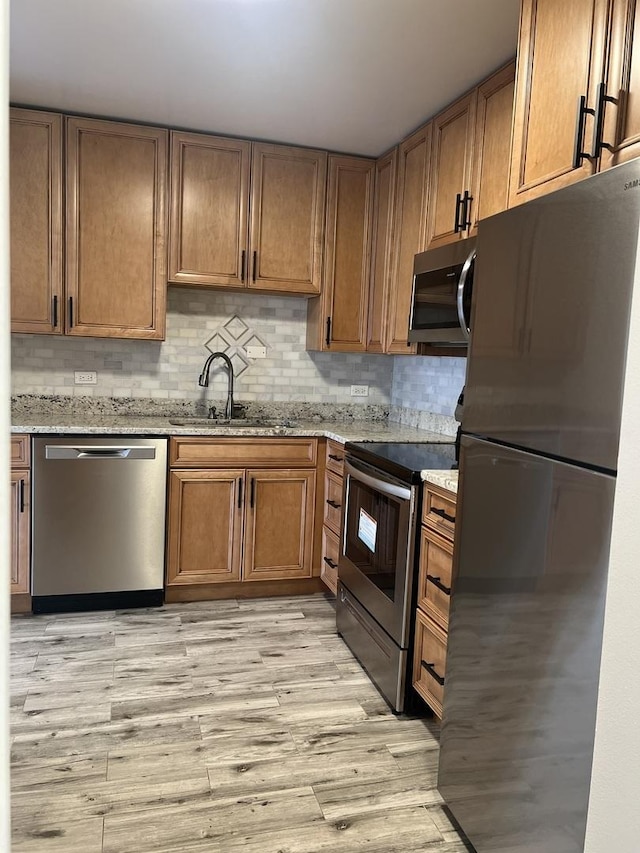 kitchen featuring appliances with stainless steel finishes, a sink, light wood-type flooring, light stone countertops, and decorative backsplash