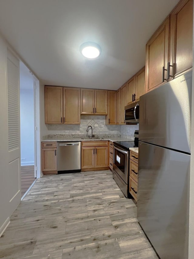 kitchen featuring stainless steel appliances, light wood-style floors, a sink, decorative backsplash, and baseboards