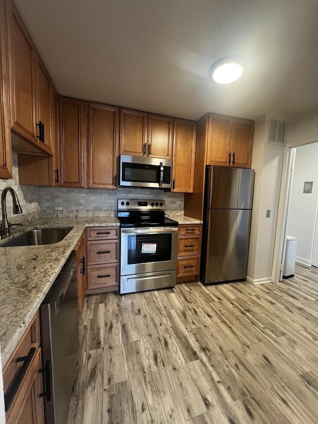 kitchen featuring appliances with stainless steel finishes, a sink, light wood finished floors, backsplash, and brown cabinets