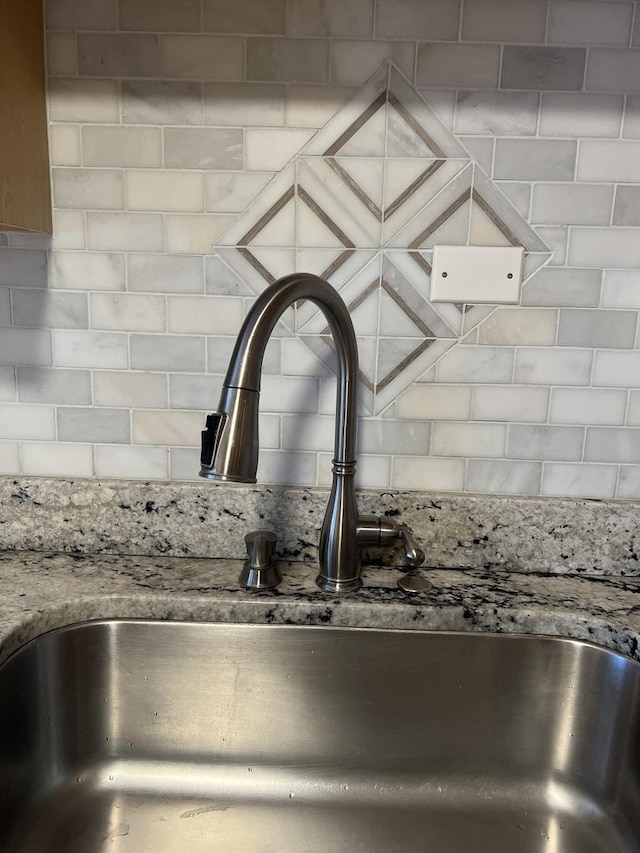 kitchen view of a sink, decorative backsplash, and light stone counters
