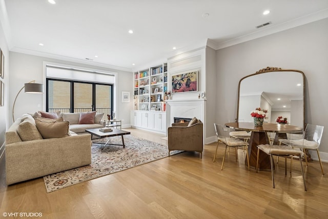 living area with crown molding, wood finished floors, baseboards, a lit fireplace, and recessed lighting