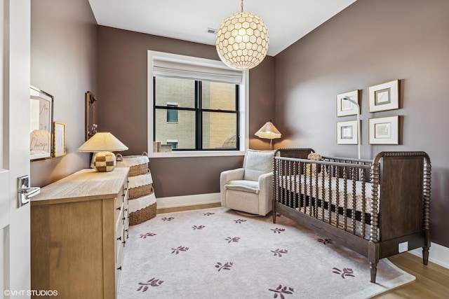 bedroom featuring a nursery area, wood finished floors, and baseboards