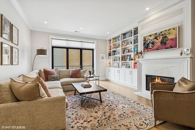 living area with a high end fireplace, light wood-style floors, recessed lighting, built in shelves, and ornamental molding
