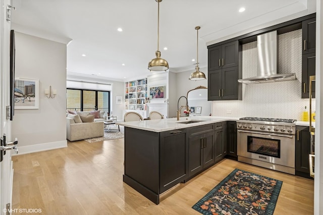 kitchen with stainless steel stove, wall chimney exhaust hood, a sink, a peninsula, and light countertops