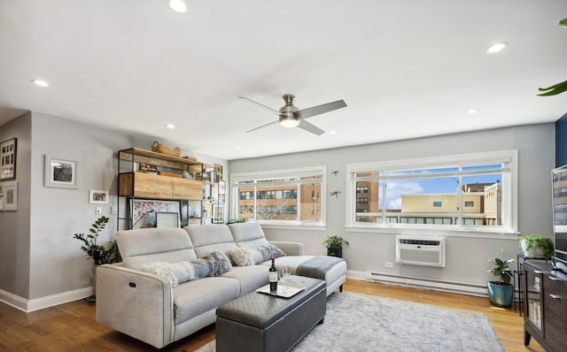 living area with a baseboard heating unit, a wall unit AC, wood finished floors, ceiling fan, and baseboards