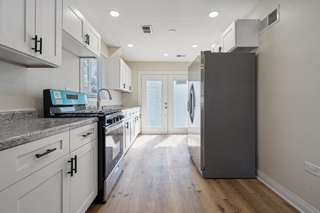 kitchen featuring appliances with stainless steel finishes, light wood finished floors, french doors, white cabinetry, and a sink