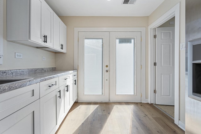 kitchen with french doors, light wood finished floors, white cabinetry, and light countertops