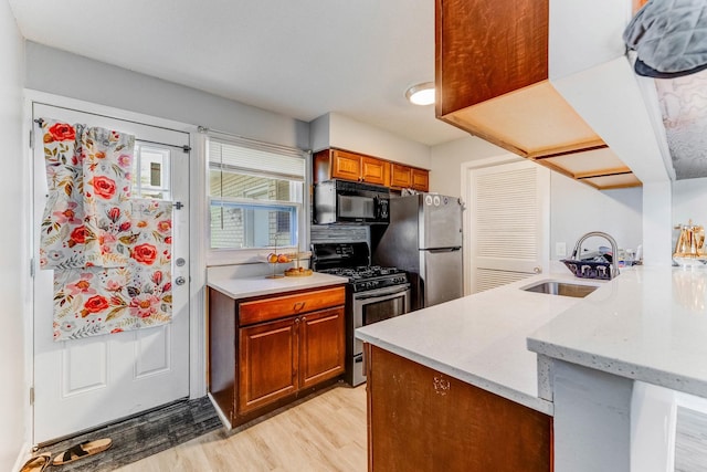 kitchen with appliances with stainless steel finishes, a sink, a peninsula, light wood finished floors, and brown cabinetry