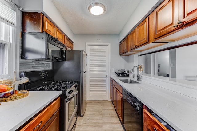 kitchen featuring black appliances, a sink, brown cabinets, light wood-type flooring, and a textured ceiling