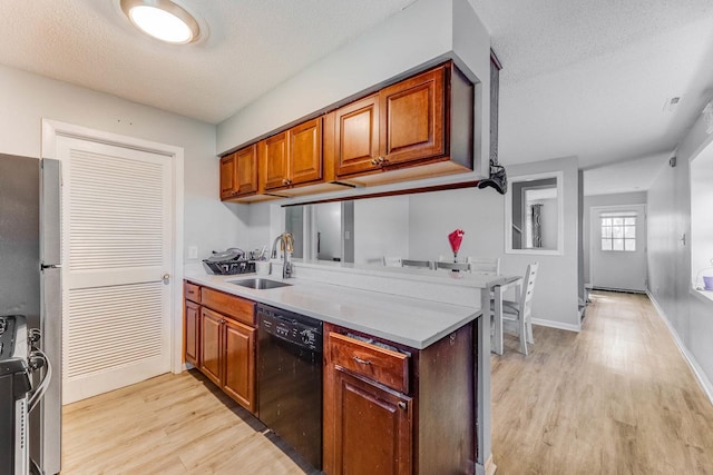 kitchen featuring appliances with stainless steel finishes, a sink, light wood finished floors, a peninsula, and a textured ceiling