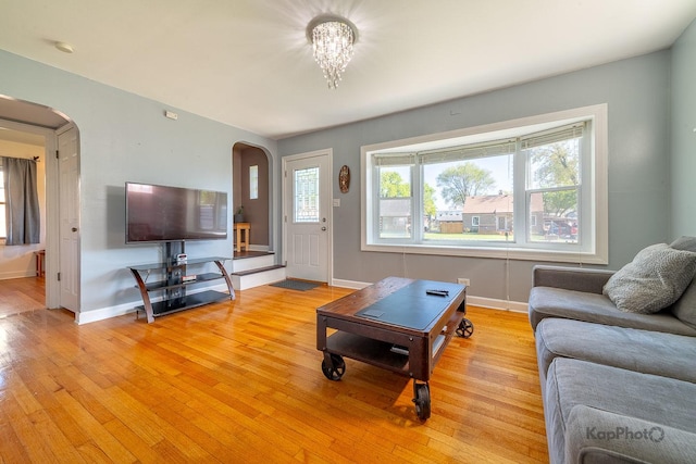 living area featuring arched walkways, light wood-style flooring, baseboards, and a chandelier