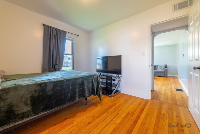 bedroom with light wood finished floors, arched walkways, and baseboards