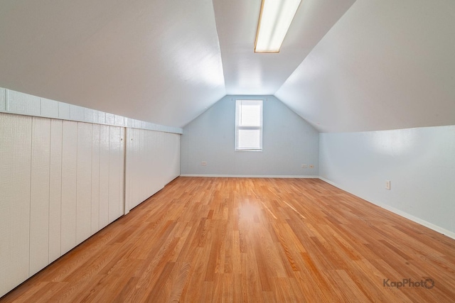 additional living space featuring light wood-style floors, vaulted ceiling, and baseboards