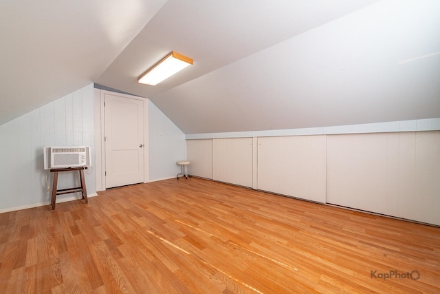 additional living space featuring light wood finished floors, vaulted ceiling, a wall mounted air conditioner, and wood walls