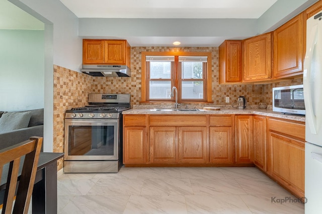 kitchen with appliances with stainless steel finishes, under cabinet range hood, a sink, and light marble finish flooring