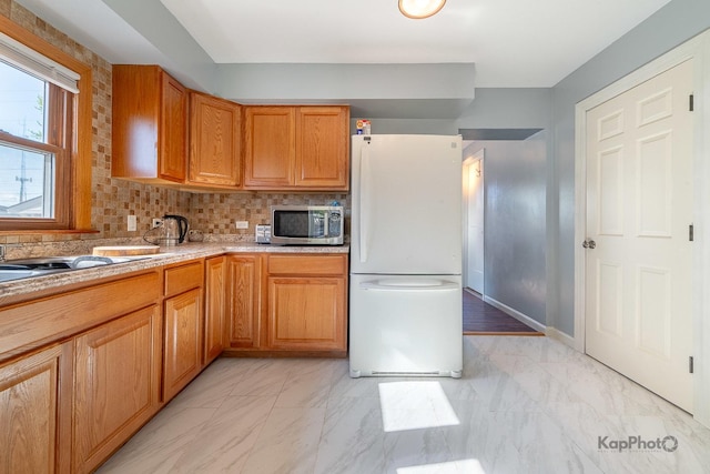 kitchen featuring freestanding refrigerator, stainless steel microwave, light marble finish flooring, light countertops, and tasteful backsplash