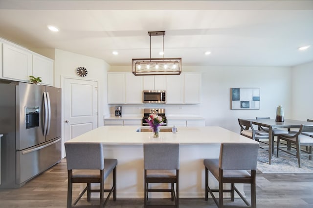 kitchen with appliances with stainless steel finishes, a kitchen breakfast bar, dark wood-style flooring, white cabinets, and recessed lighting