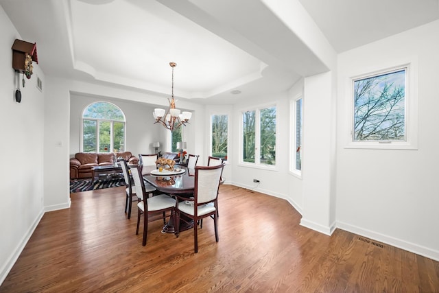 dining area with a tray ceiling, wood finished floors, a chandelier, and baseboards