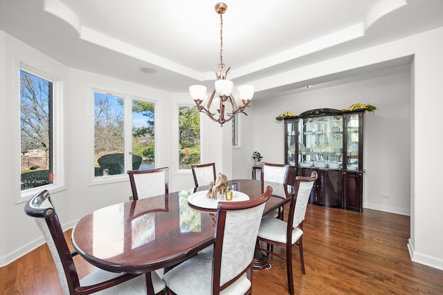 dining space with a raised ceiling, wood finished floors, a chandelier, and baseboards