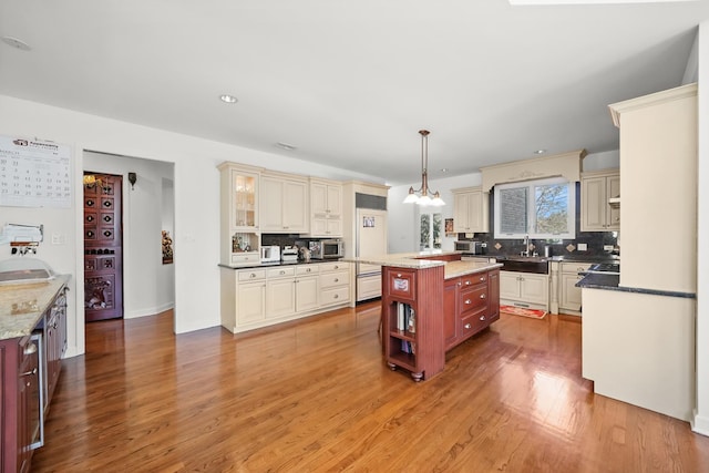 kitchen with cream cabinets, tasteful backsplash, light wood-style flooring, stainless steel microwave, and recessed lighting