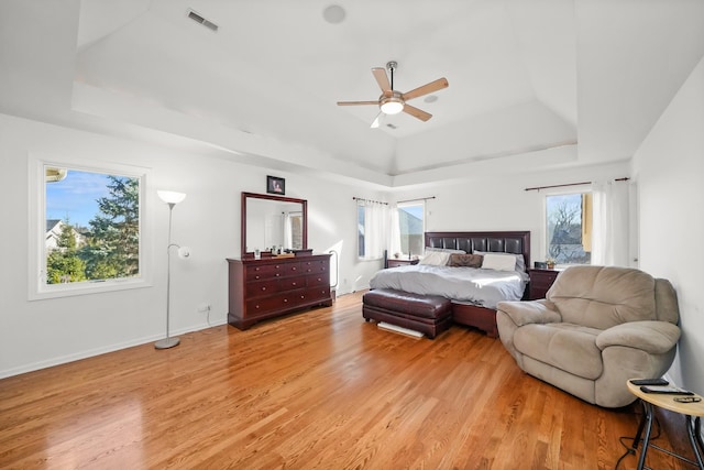 bedroom featuring a raised ceiling, light wood-type flooring, multiple windows, and baseboards