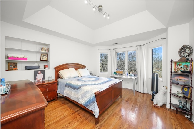 bedroom with light wood-type flooring and a tray ceiling