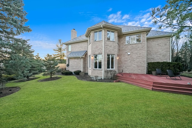 back of property featuring a chimney, a deck, brick siding, and a yard