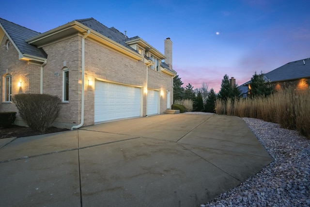 view of side of home with brick siding, concrete driveway, a chimney, and an attached garage