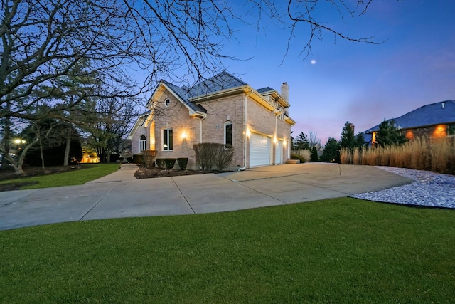 property exterior at dusk with a chimney, concrete driveway, a garage, and a lawn