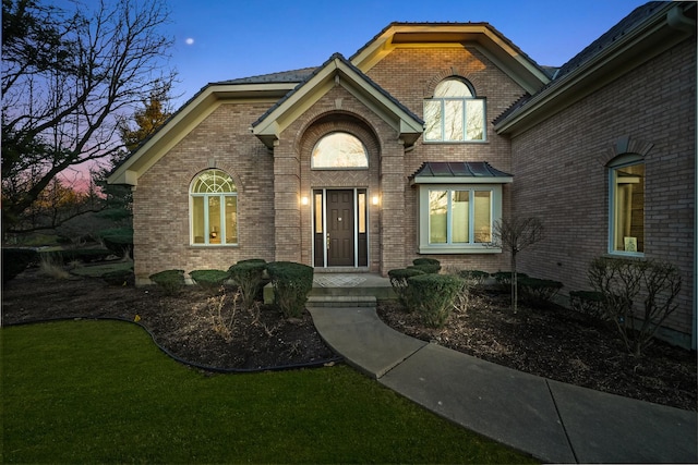 property entrance with brick siding, a lawn, and a standing seam roof