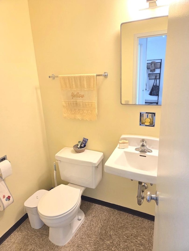 half bath with toilet, baseboards, and a sink