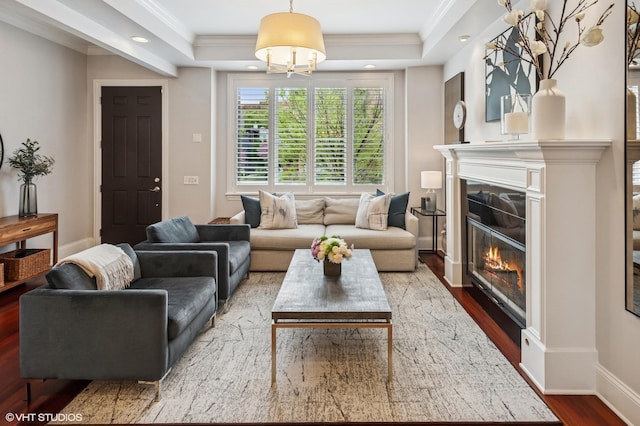 living area with wood finished floors, crown molding, a glass covered fireplace, recessed lighting, and baseboards