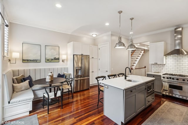 kitchen featuring appliances with stainless steel finishes, wall chimney range hood, a sink, gray cabinetry, and a kitchen bar