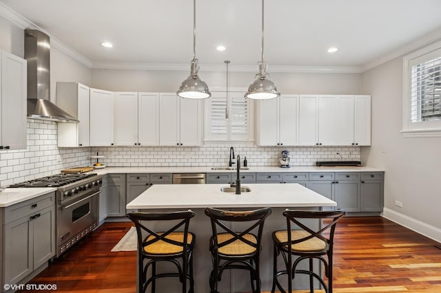 kitchen with gray cabinetry, appliances with stainless steel finishes, wall chimney range hood, a sink, and light countertops